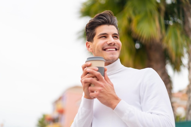 Giovane uomo caucasico all'aperto che tiene un caffè da asporto e ha dubbi