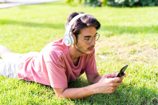 Giovane uomo caucasico all'aperto in un parco che ascolta musica con il cellulare