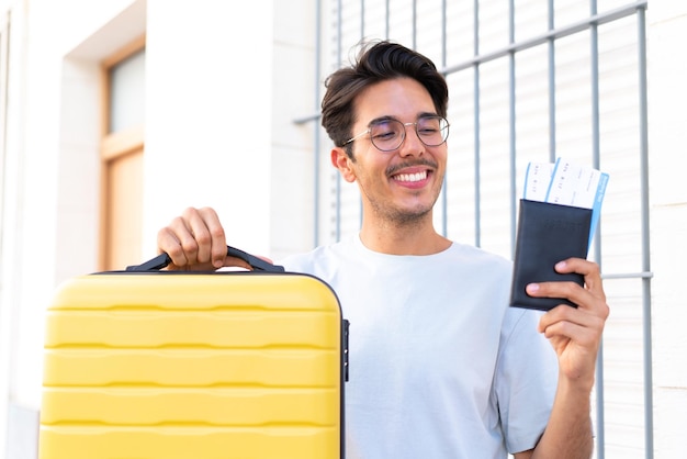 Giovane uomo caucasico all'aperto in vacanza con valigia e passaporto