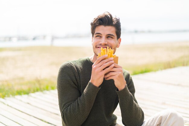 Giovane uomo caucasico all'aperto prendendo patatine fritte