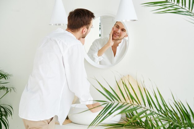 Giovane uomo caucasico attraente che tocca godendosi il viso allo specchio e sorridendo in primo piano Concetto di cura della pelle