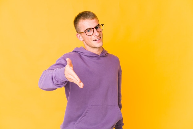 Giovane uomo caucasico bello che allunga la mano alla macchina fotografica nel gesto di saluto.