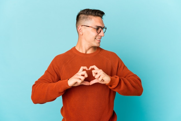 Giovane uomo caucasico bello isolato sorridendo e mostrando una forma di cuore con le mani.