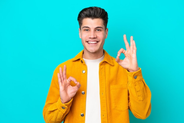 Giovane uomo caucasico bello isolato su bakcground blu che mostra segno giusto con due mani
