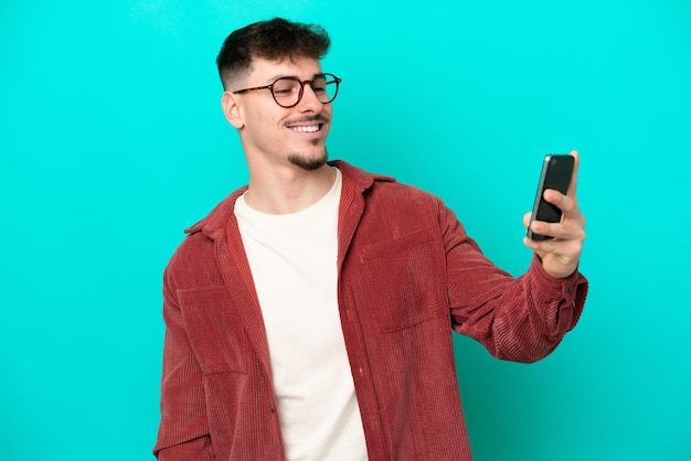 Giovane uomo caucasico bello isolato su priorità bassa blu che fa un selfie