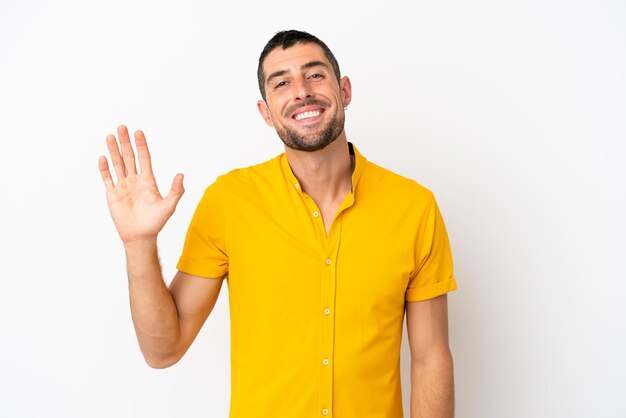 Giovane uomo caucasico bello isolato su sfondo bianco salutando con la mano con felice espressione