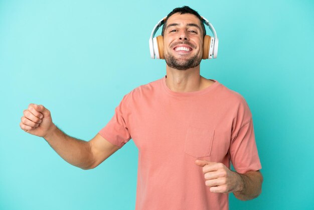 Giovane uomo caucasico bello isolato su sfondo blu ascoltando musica e ballando