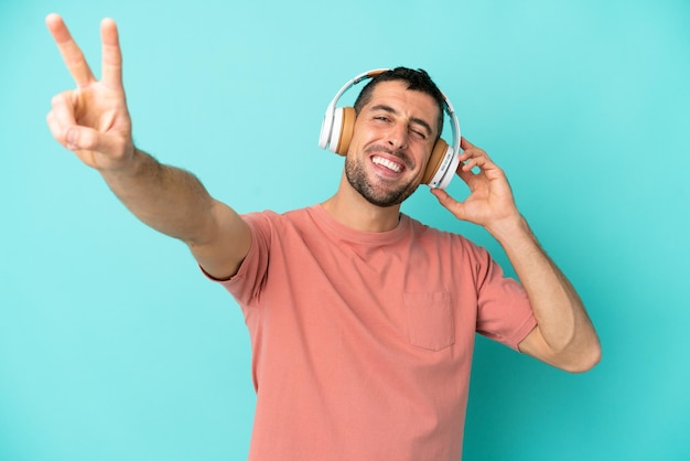 Giovane uomo caucasico bello isolato su sfondo blu ascoltando musica e cantando