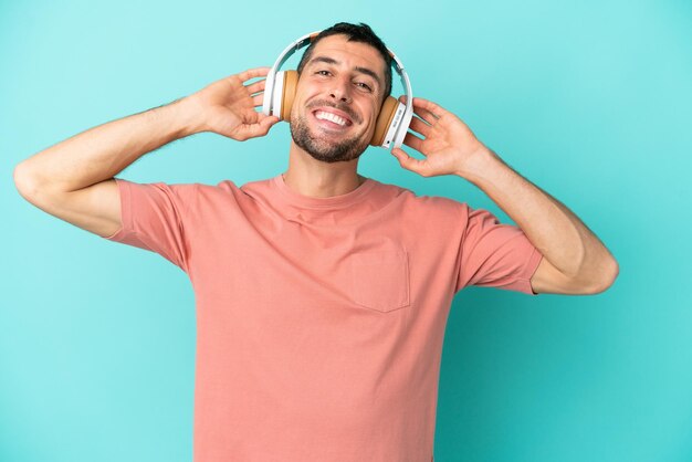 Giovane uomo caucasico bello isolato su sfondo blu ascoltando musica