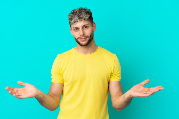 Giovane uomo caucasico bello isolato su sfondo blu che ha dubbi