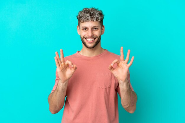 Giovane uomo caucasico bello isolato su sfondo blu che mostra segno ok con due mani