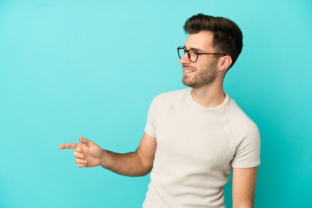 Giovane uomo caucasico bello isolato su sfondo blu che punta il dito di lato e presenta un prodotto