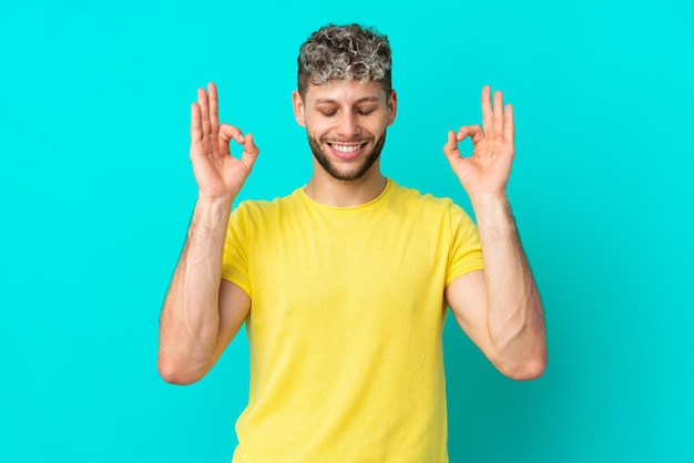 Giovane uomo caucasico bello isolato su sfondo blu in posa zen