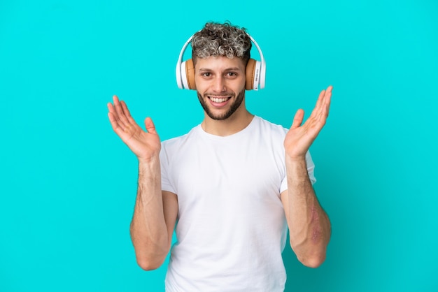 Giovane uomo caucasico bello isolato su sfondo blu sorpreso e ascoltando musica