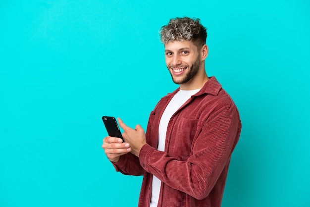 Giovane uomo caucasico bello isolato su sfondo blu utilizzando il telefono cellulare e puntando indietro