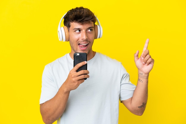 Giovane uomo caucasico bello isolato su sfondo giallo ascoltando musica con un cellulare e cantando