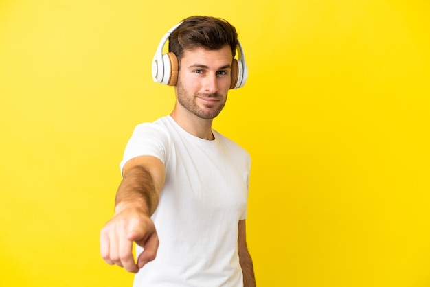 Giovane uomo caucasico bello isolato su sfondo giallo ascoltando musica