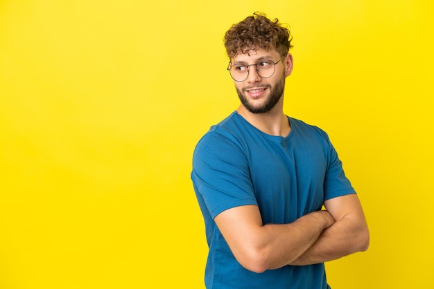 Giovane uomo caucasico bello isolato su sfondo giallo che guarda al lato e sorridente