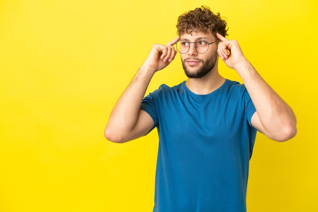 Giovane uomo caucasico bello isolato su sfondo giallo che ha dubbi e pensa