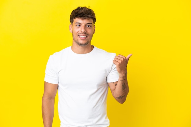 Giovane uomo caucasico bello isolato su sfondo giallo che punta al lato per presentare un prodotto