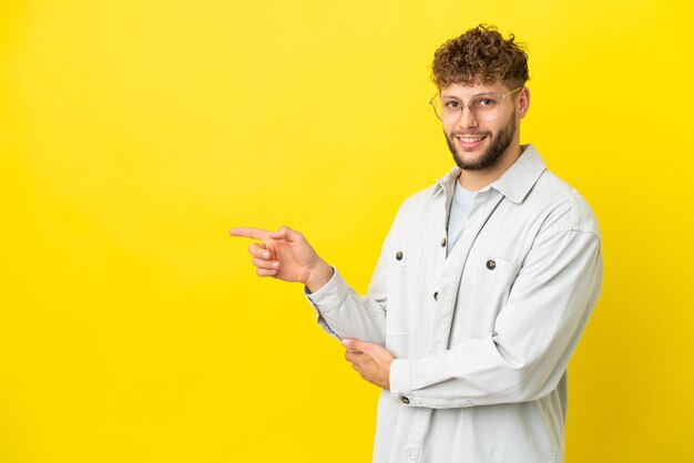 Giovane uomo caucasico bello isolato su sfondo giallo che punta il dito di lato