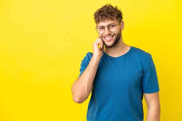 Giovane uomo caucasico bello isolato su sfondo giallo ridendo