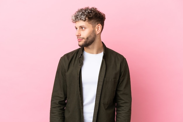 Giovane uomo caucasico bello isolato su sfondo rosa che guarda di lato