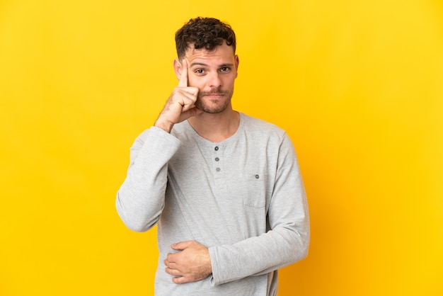 Giovane uomo caucasico bello isolato sulla parete gialla che pensa un'idea