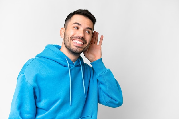 Giovane uomo caucasico bello su sfondo bianco isolato ascoltando qualcosa mettendo la mano sull'orecchio