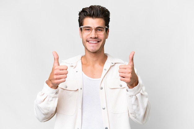 Giovane uomo caucasico bello su sfondo bianco isolato con il pollice in alto gesto e sorridente