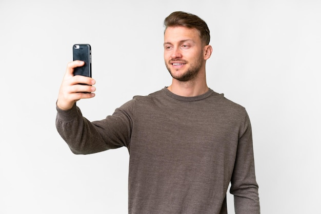 Giovane uomo caucasico bello su sfondo bianco isolato facendo un selfie