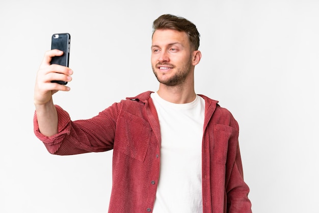 Giovane uomo caucasico bello su sfondo bianco isolato facendo un selfie