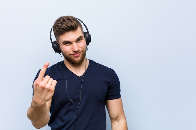 Giovane uomo caucasico che ascolta la musica che punta con il dito su di te come se invitando ad avvicinarsi.