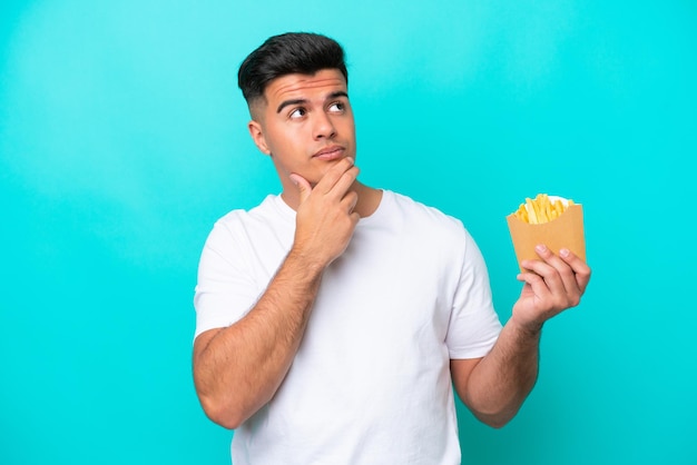 Giovane uomo caucasico che cattura patatine fritte isolate su sfondo blu con dubbi