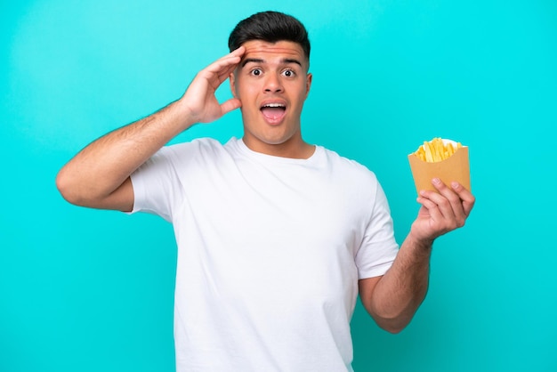 Giovane uomo caucasico che cattura patatine fritte isolate su sfondo blu con espressione a sorpresa