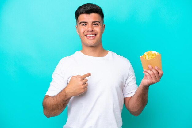 Giovane uomo caucasico che cattura patatine fritte isolate su sfondo blu con espressione facciale a sorpresa