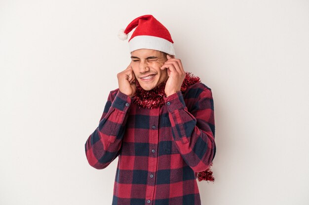 Giovane uomo caucasico che celebra il Natale isolato su sfondo bianco che copre le orecchie con le mani.