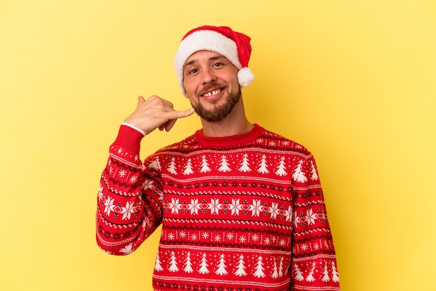 Giovane uomo caucasico che celebra il Natale isolato su sfondo giallo che mostra un gesto di telefonata con le dita.