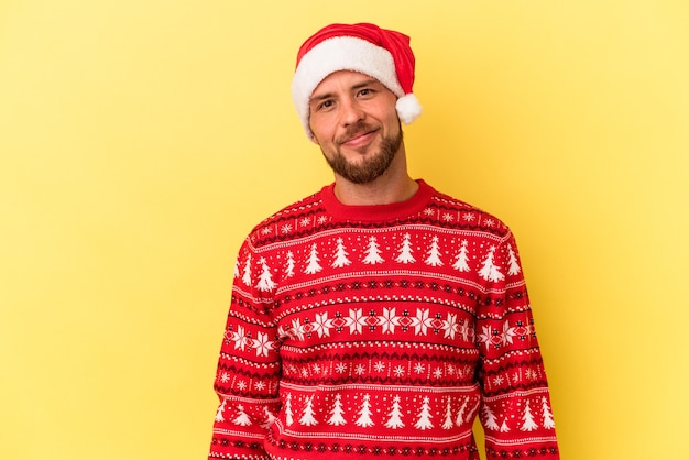 Giovane uomo caucasico che celebra il Natale isolato su sfondo giallo felice, sorridente e allegro.