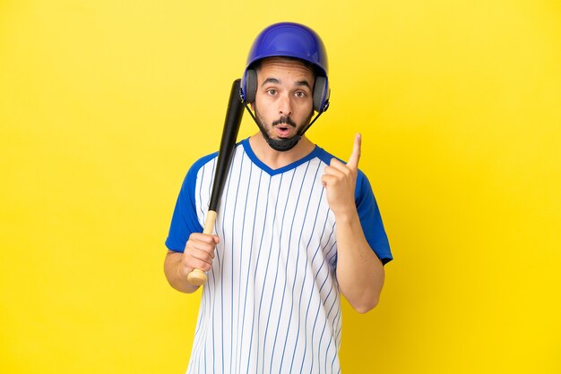 Giovane uomo caucasico che gioca a baseball isolato su sfondo giallo con l'intenzione di realizzare la soluzione sollevando un dito