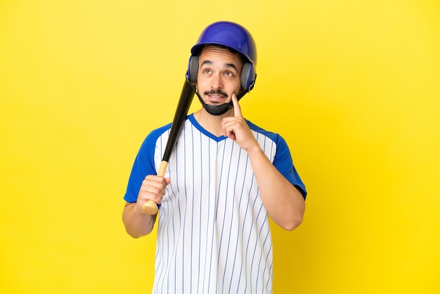 Giovane uomo caucasico che gioca a baseball isolato su sfondo giallo pensando a un'idea mentre guarda in alto