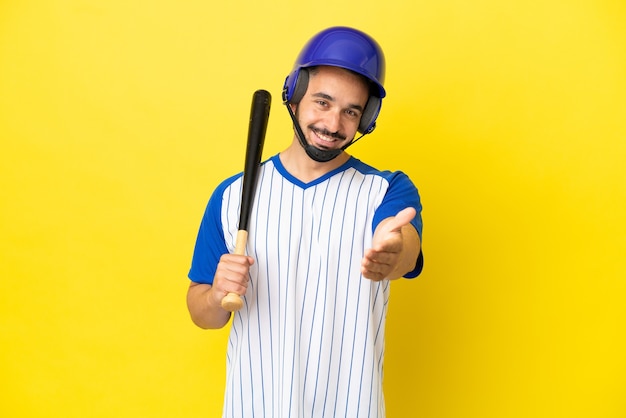 Giovane uomo caucasico che gioca a baseball isolato su sfondo giallo stringe la mano per aver chiuso un buon affare