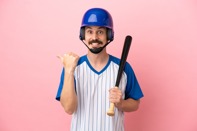 Giovane uomo caucasico che gioca a baseball isolato su sfondo rosa che punta al lato per presentare un prodotto