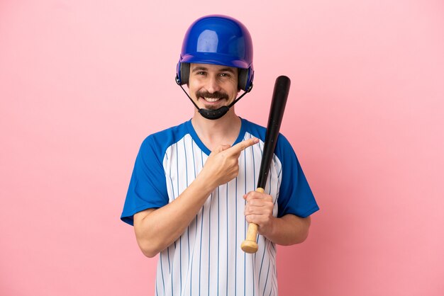 Giovane uomo caucasico che gioca a baseball isolato su sfondo rosa che punta al lato per presentare un prodotto