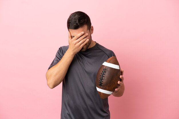 Giovane uomo caucasico che gioca a rugby isolato su sfondo rosa con espressione stanca e malata