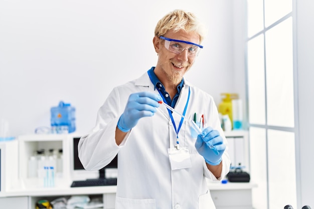 Giovane uomo caucasico che indossa l'uniforme da scienziato utilizzando la pipetta in laboratorio