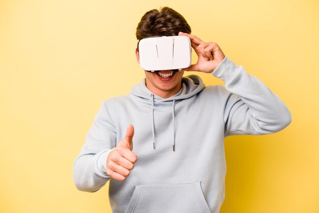 Giovane uomo caucasico che indossa occhiali virtuali isolati su sfondo giallo