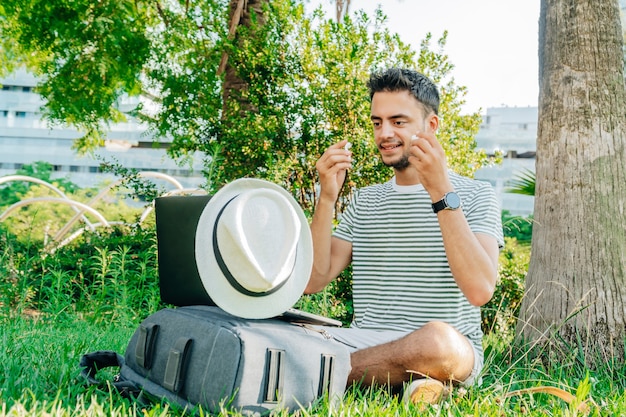 Giovane uomo caucasico che indossa un auricolare wireless seduto sull'erba.