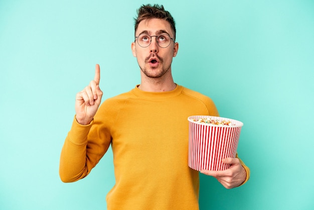 Giovane uomo caucasico che mangia popcorn isolato su sfondo blu rivolto verso l'alto con la bocca aperta.