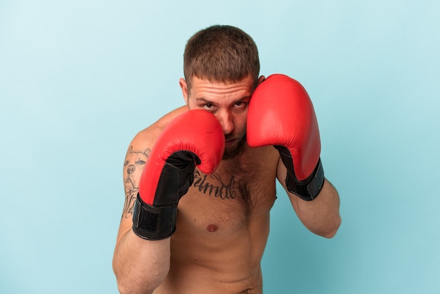 Giovane uomo caucasico che pratica boxe isolato su sfondo blu